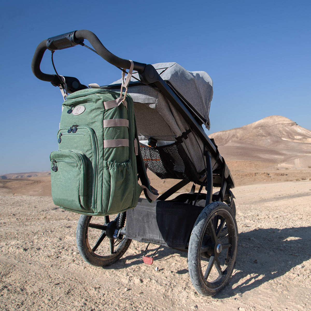 A Fledgling bag hangs from the handlebars of a jogging stroller in the middle of a desert hike.